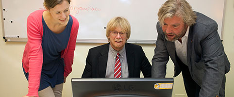 zwei Männer und eine Frauen schauen auf Bildschirm