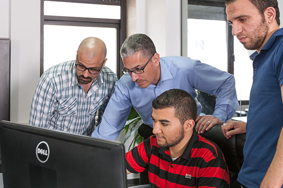 four German and Arab men working together at a computer