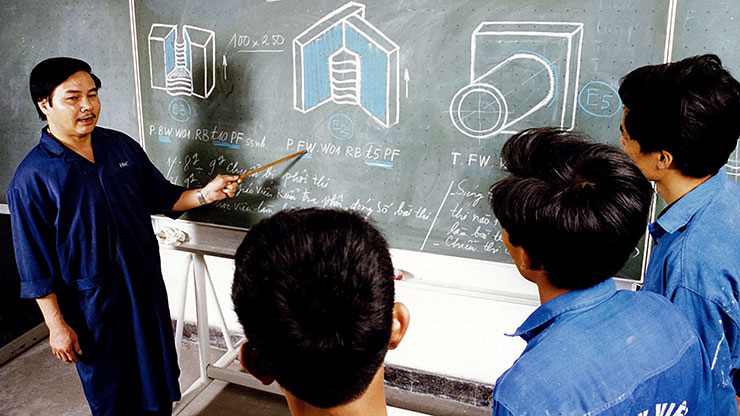 teacher explains various technical drawings to students on a blackboard