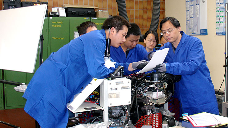 several Chinese trainees in blue overalls being trained on a machine