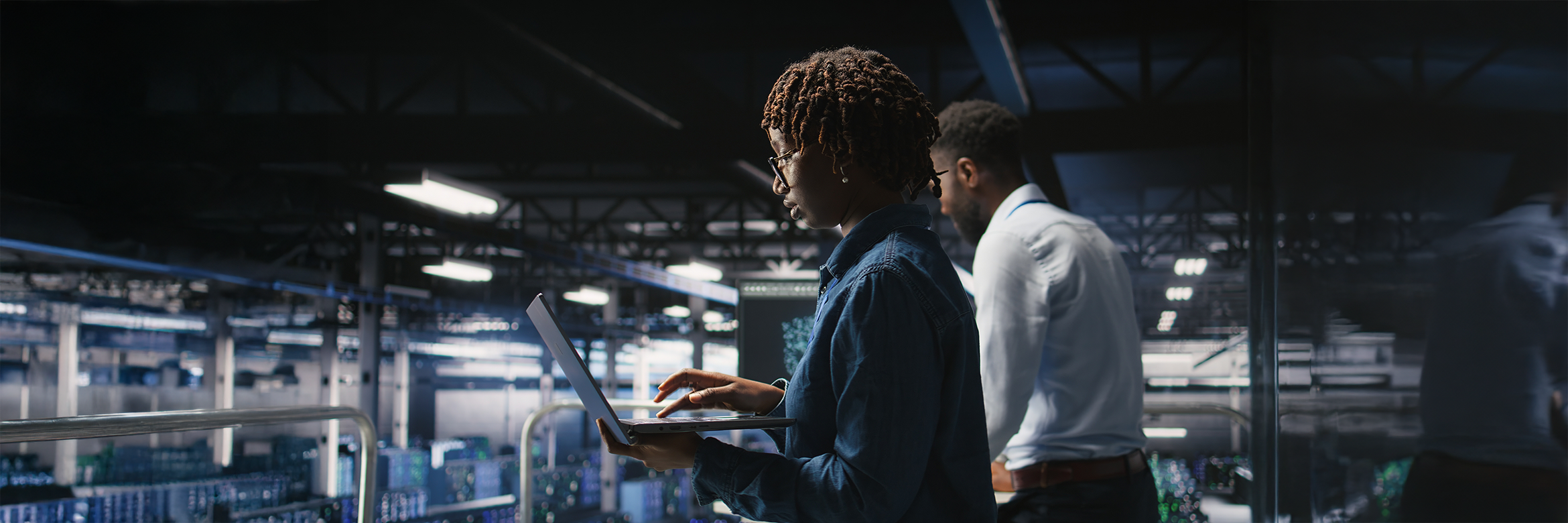 junge Frau mit Laptop im Vordergrunf, dahinter junger Mann, IT Arbeitsumgebung