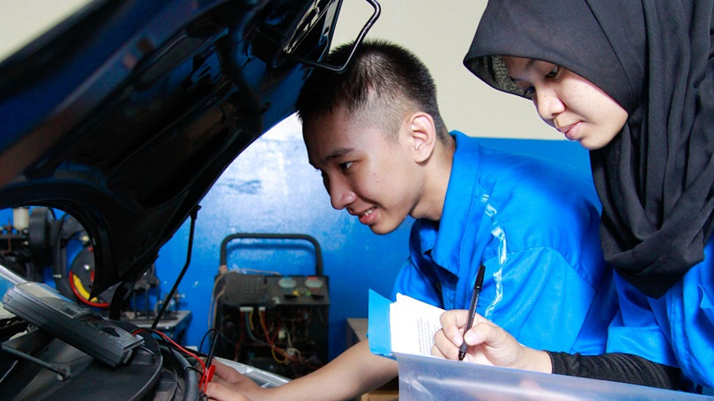 Indonesier und Indonesierin beugen sich über einen Automotor