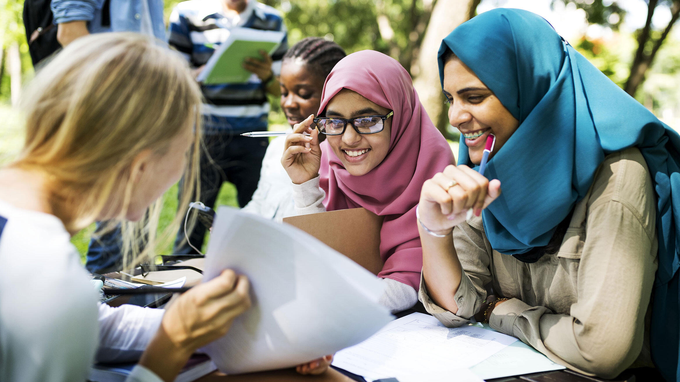 zwei Malaysierinnen und eine Europäerin sitzen am Tisch und schauen in Papiere