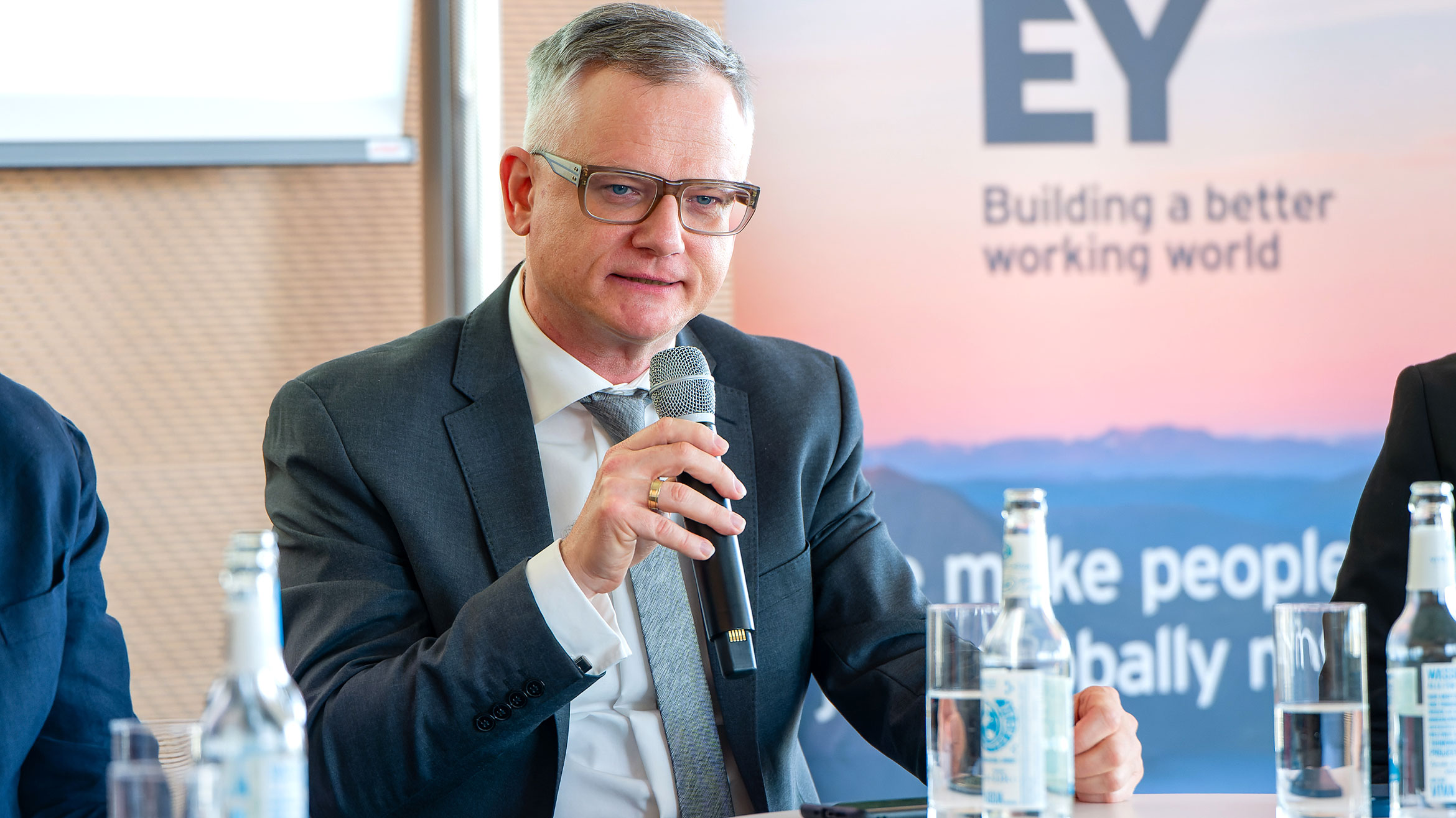 Mann sitzt auf dem Podium und spricht in ein Mikrofon