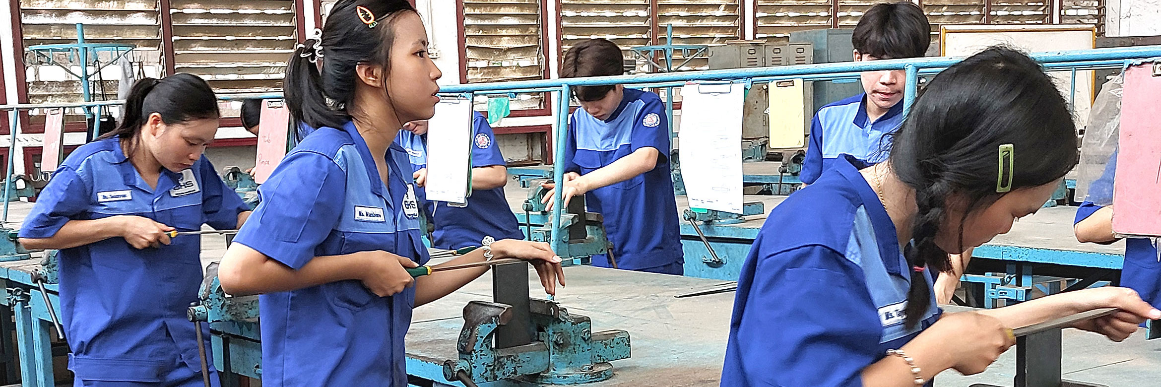 mehrere laotische junge Männer und Frauen bearbeiten Metallstücke mit Metallfeilen