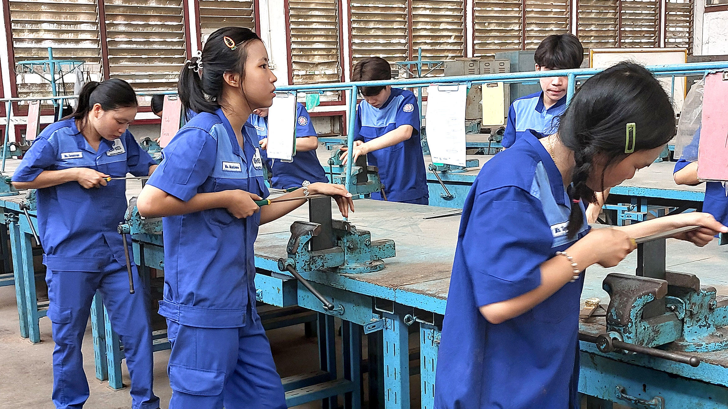 mehrere laotische junge Männer und Frauen bearbeiten Metallstücke mit einer Metallfeile