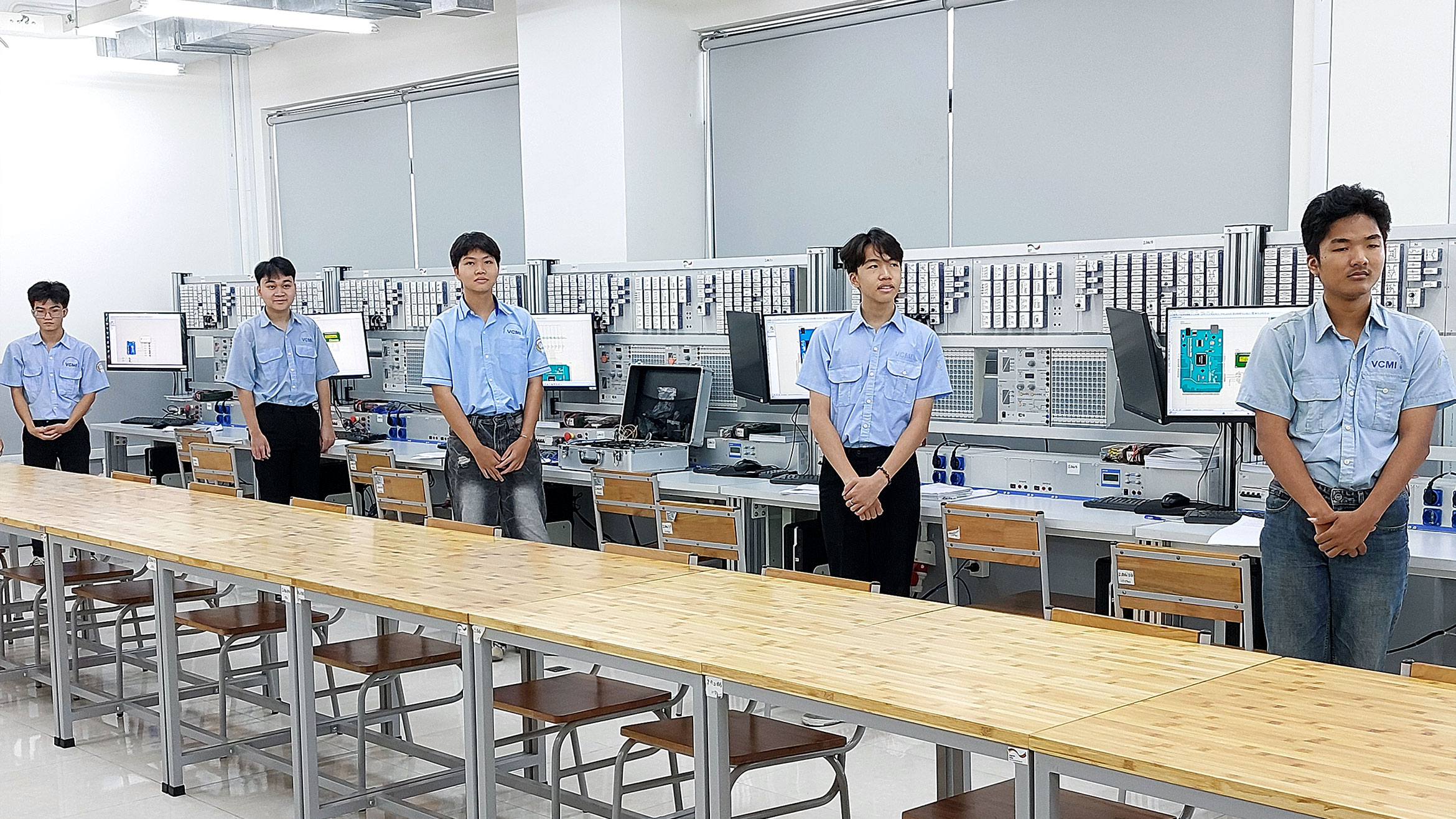 vier junge Vietnamesen stehen an ihren Computer-Arbeitsplätzen und schauen in dieselbe Richtung