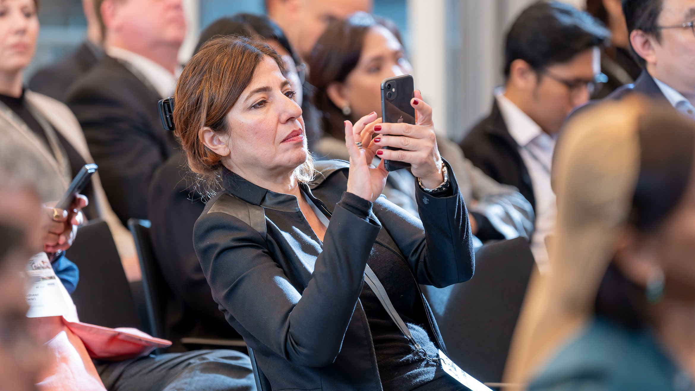 Blick in den Zuhörersaal, eine Frau fotografiert oder filmt mit dem Handy
