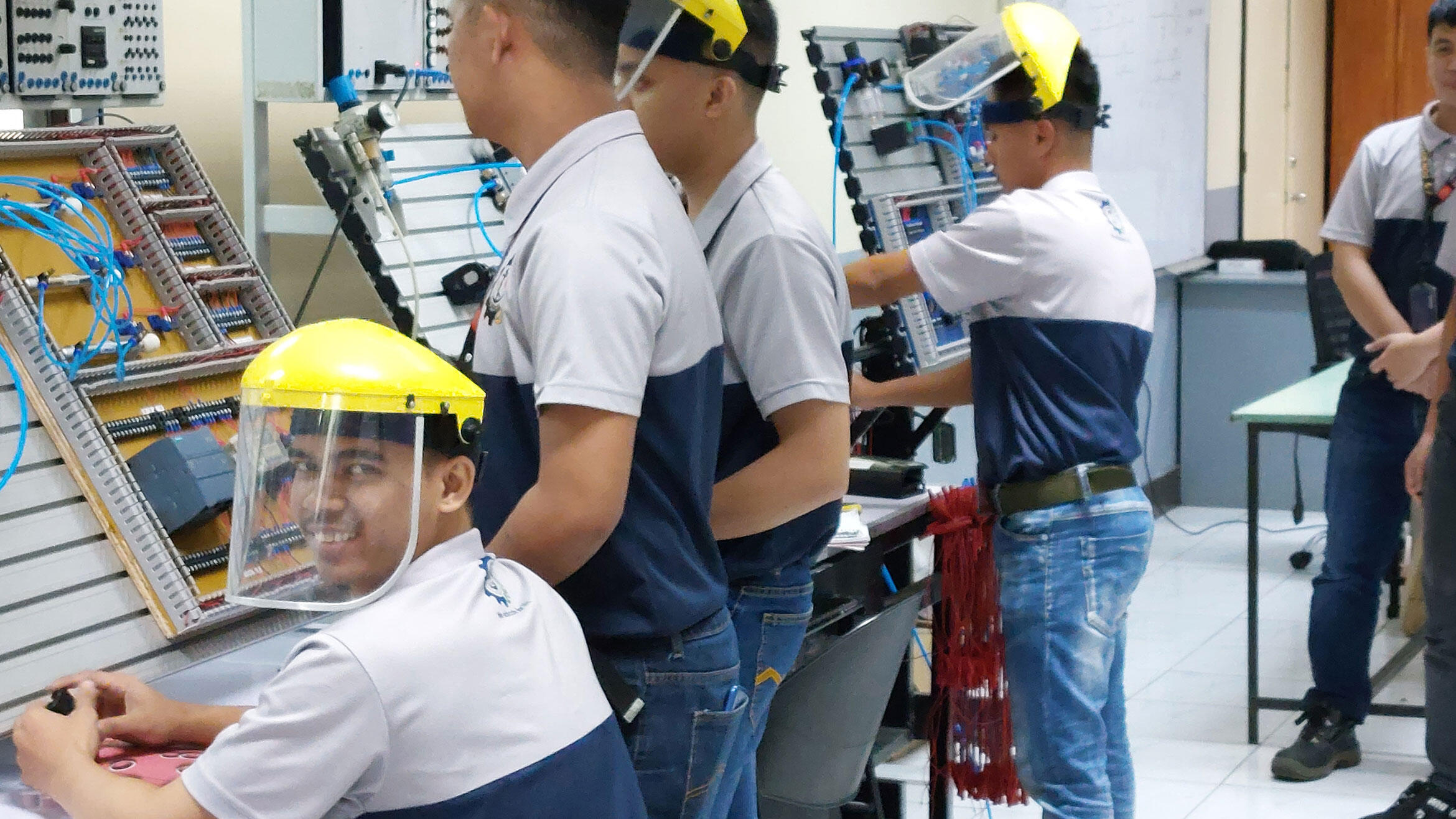 junge Männer mit Helm und Gesichtsschutz üben an Arbeitswänden mit Elektronikaufbau