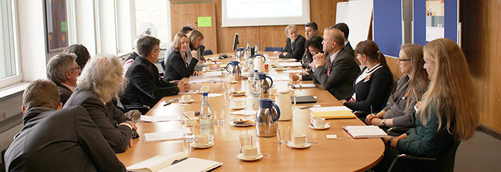Blick in den Raum: Teilnehmerinnen und Teilnehmer sitzen um den Runden Tisch