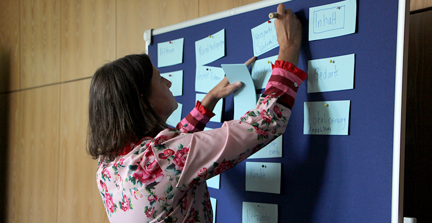 Teilnehmerin schreibt etwas auf eine Karte an einer Pinwand