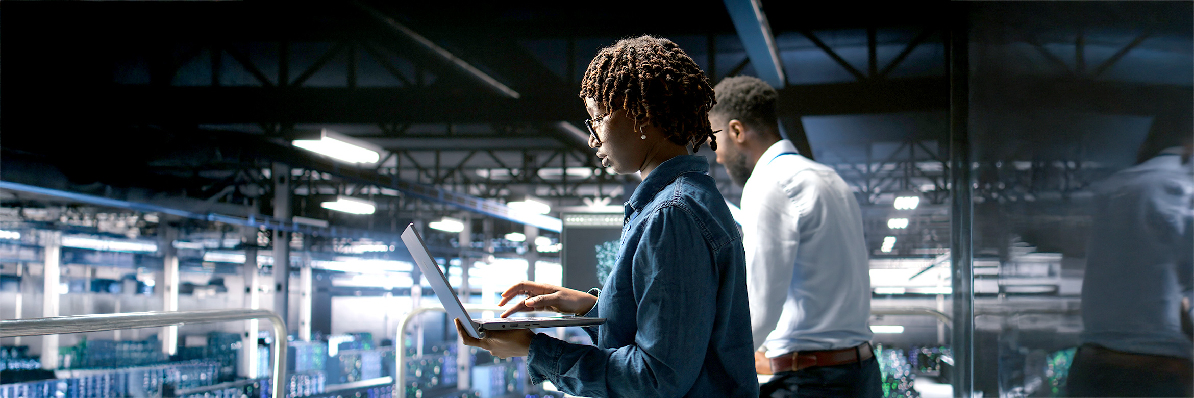 junge Frau mit Laptop im Vordergrund, dahinter junger Mann, IT Arbeitsumgebung