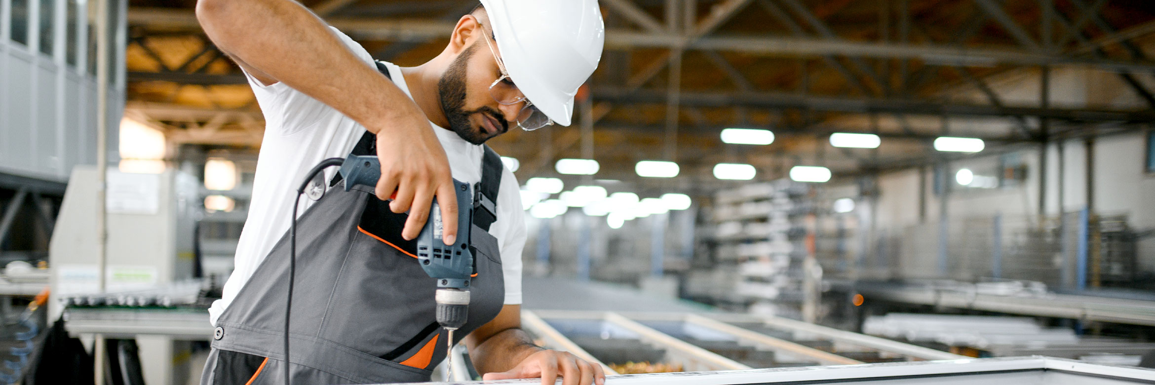 indischer Arbeiter in Arbeitskleidung und mit Schutzhelm bohrt in einen Metallrahmen