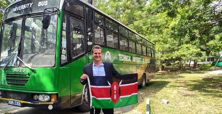 Mann steht vor Reisebus und präsentiert kenianische Nationaflagge