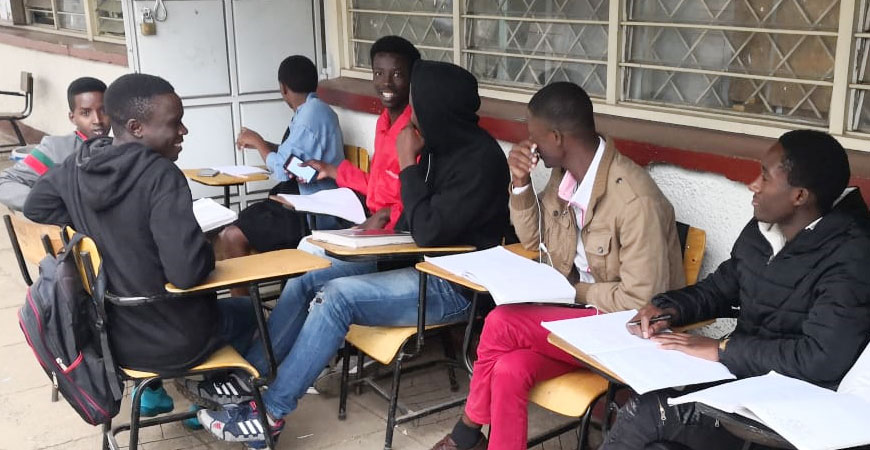 junge Kenianer sitzen vor einer Bildungseinrichtung und lernen