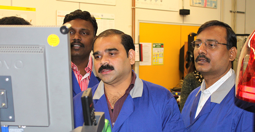 drei Inder in Arbeitskleidung schauen auf einen Bildschirm in Augenhöhe