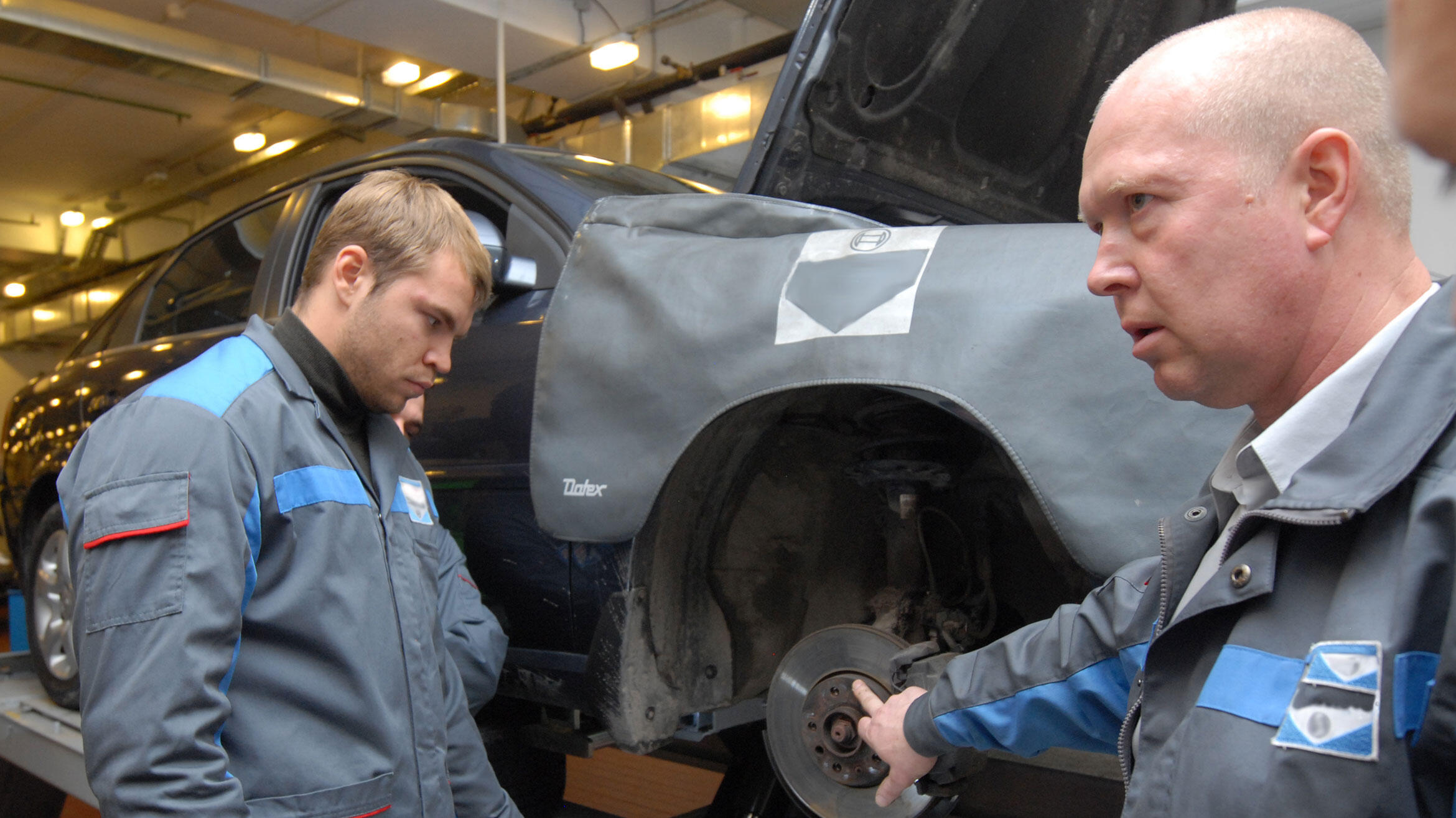 zwei Männer in Arbeitskleidung an aufgebocktem Auto