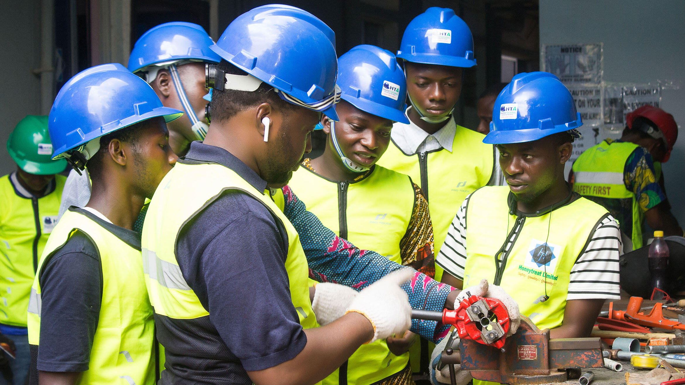 6 Nigerianer in Arbeitskleidung stehen um einen Schraubstock