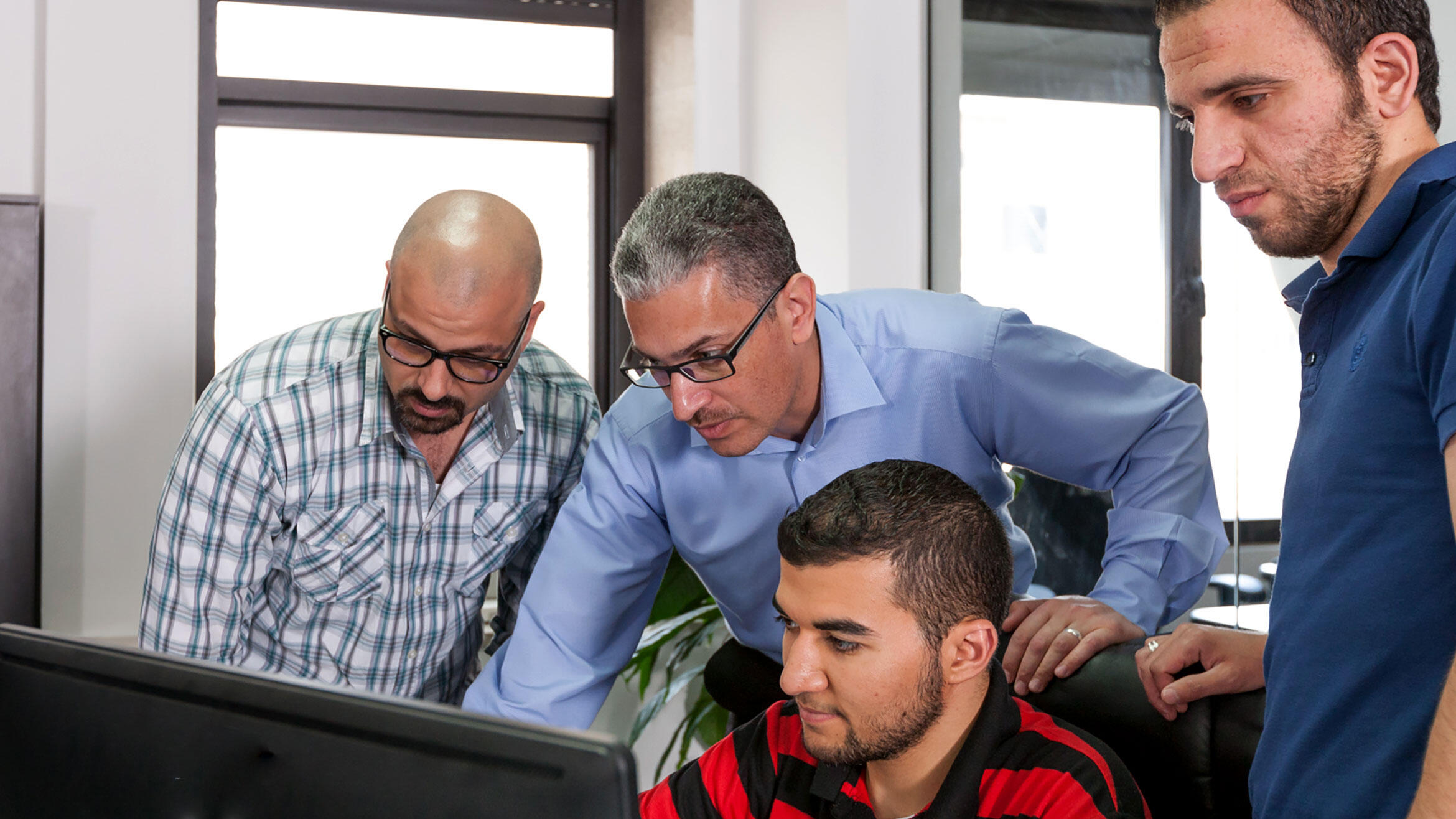 vier arabisch aussehende Männer schauen auf einen Bildschirm