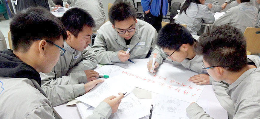 mehrere Chinesen beugen sich über einen Papierbogen auf dem Tisch, den sie beschriften