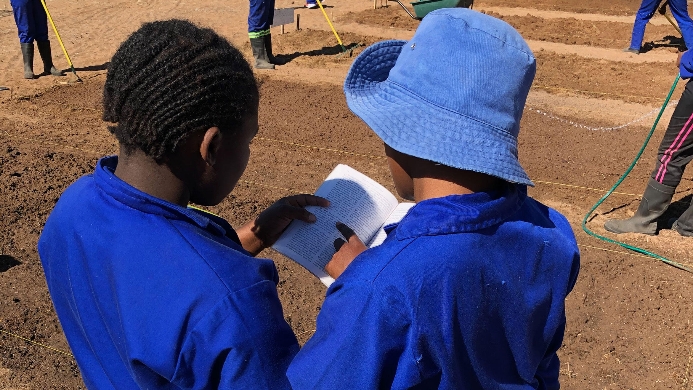 zwei namibische Auszubildende in Arbeitskleidung lesen gemeinsam in einem Buch oder einer Broschüre