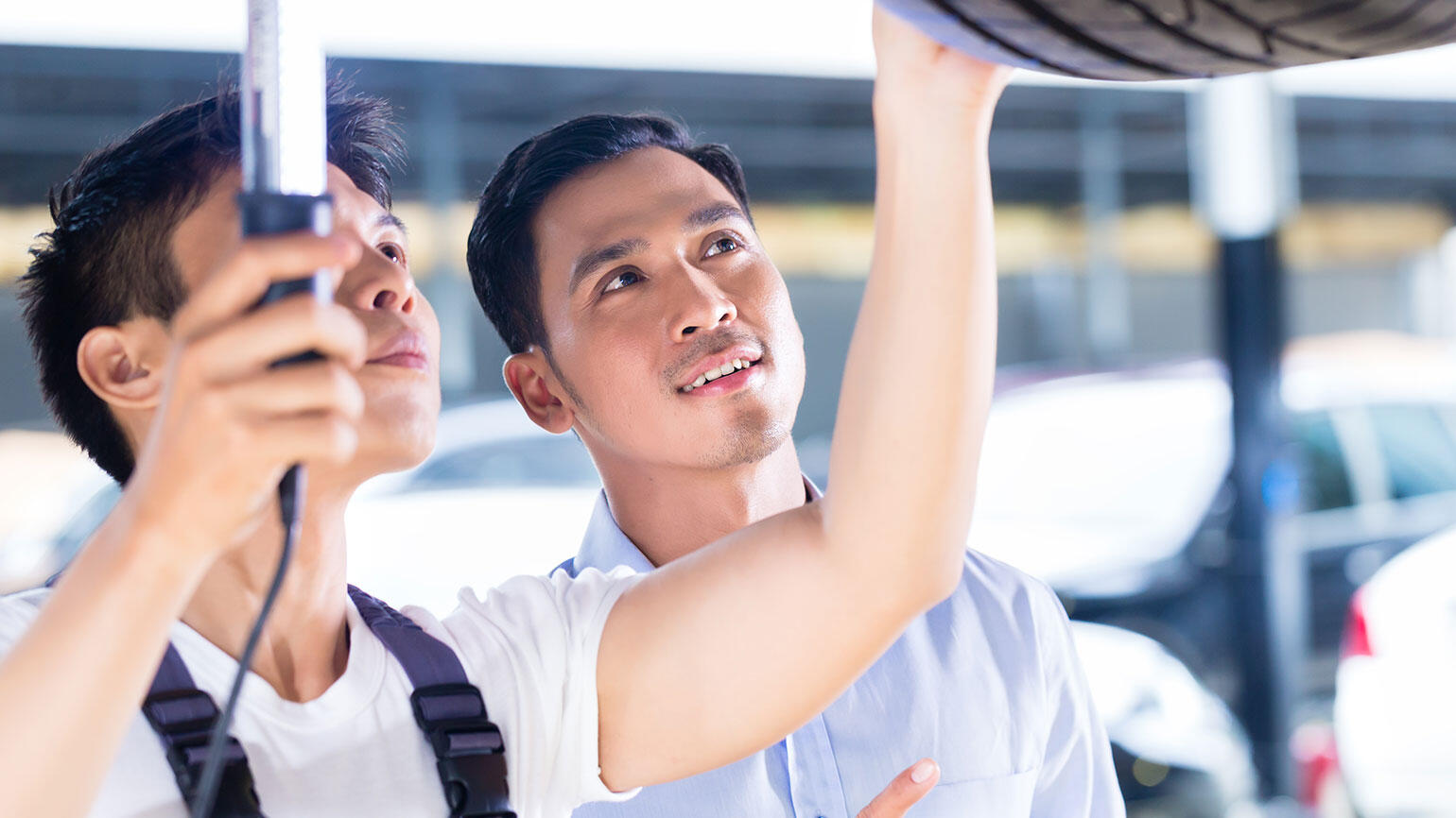 zwei mutmaßlich asiatische Männer inspizieren den Unterboden eines Autos