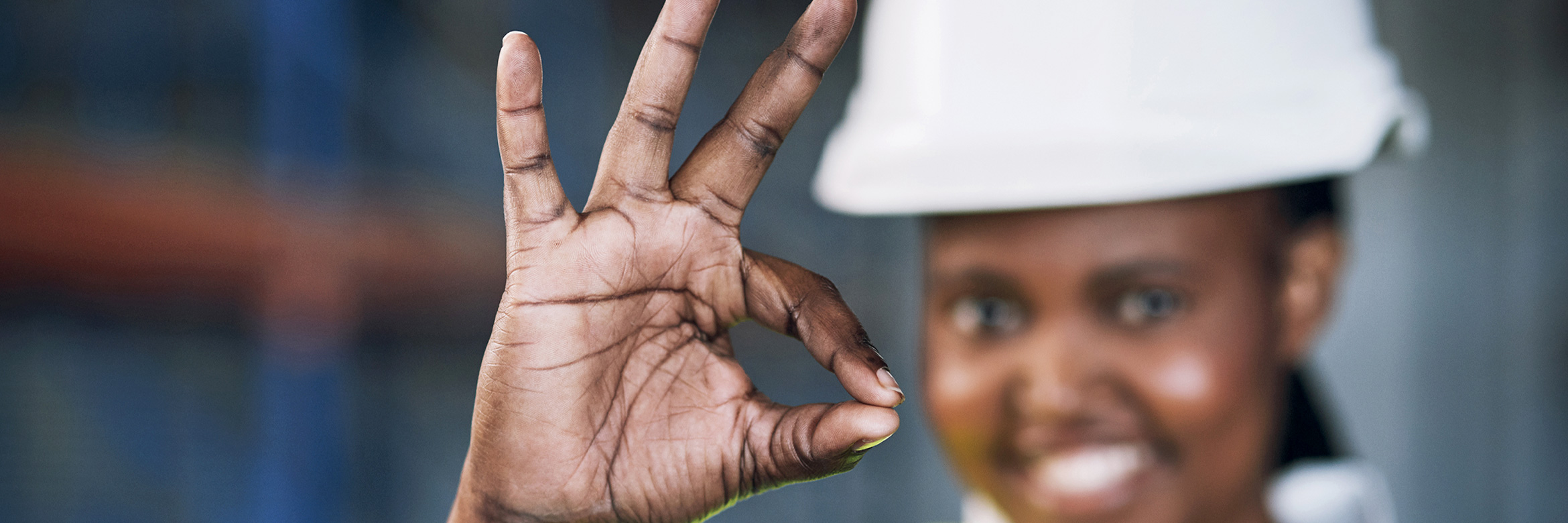 mutmaßlich afrikanische Frau trägt einen Bauhelm und formt mit einer Hand ein OK-Zeichen