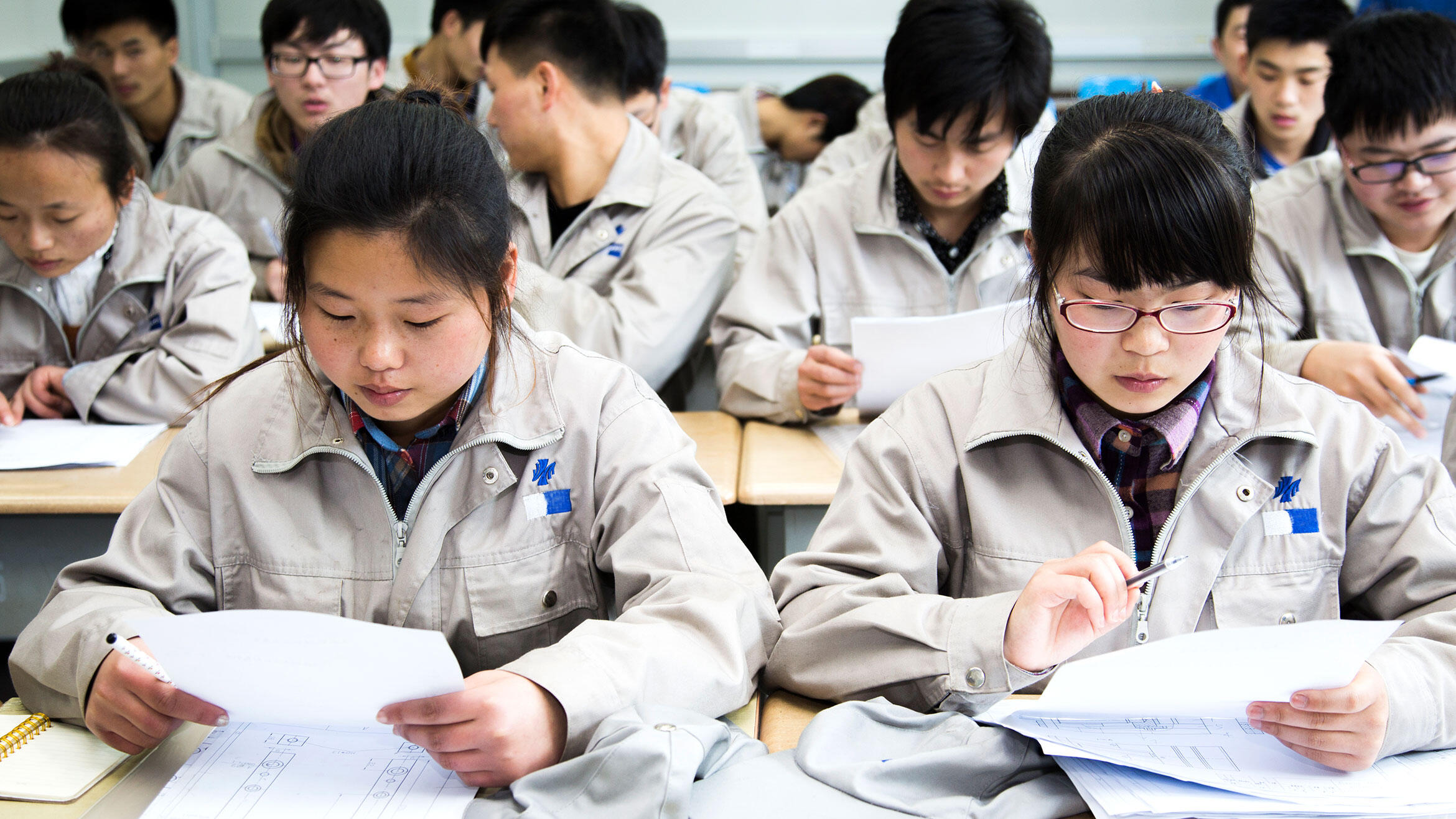 Nahaufnahme zweier Chinesinnen in Arbeitskleidung in einem Schulungsraum