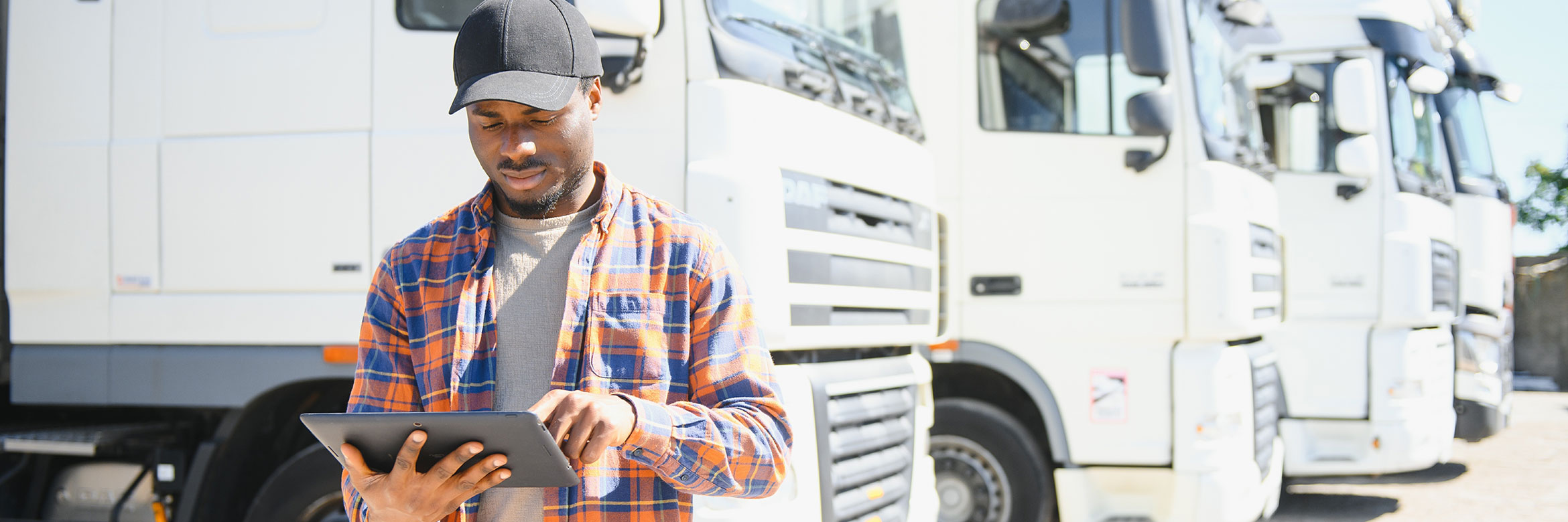 mutmaßlich afrikanischer Mann steht neben einem Lastwagen und tippt auf ein Tablet, das er in seiner Hand hält