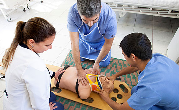 Ausbilderin übt mit zwei Männern Herzdruckmassage an einem Torso