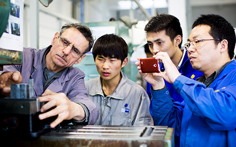 Ausbilder zeigt drei jungen asiatischen Maennern einen Arbeitsschritt