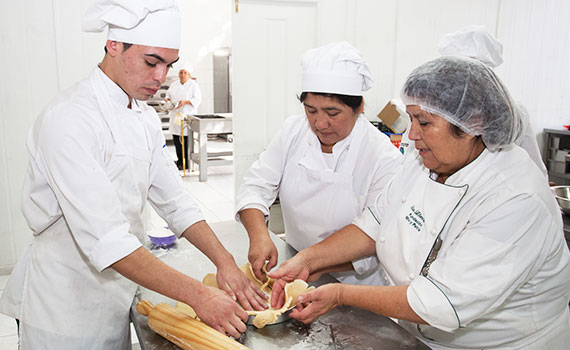 Szene einer Trainingsmaßnahme: Ausbilderin mit zwei Absolventen beim Backen