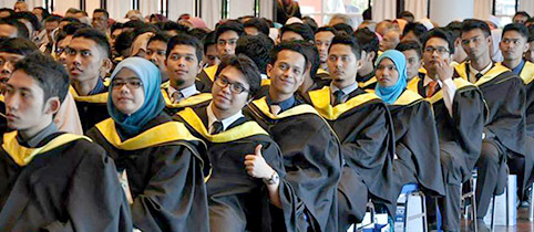Studierende sitzen in Stuhlreihen hintereinander bei Abschlussfeier