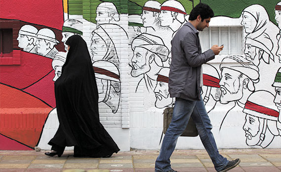 Iraner geht an einer Wand vorbei und schaut auf sein Mobiltelefon