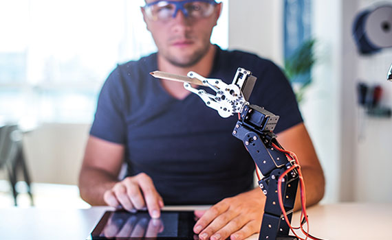 Mann benutzt Tablet und schaut auf Roboterarm
