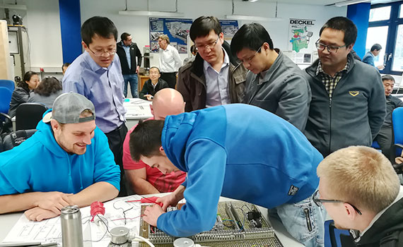 chinesische Lehrkräfte beobachten Auszubildende bei der Arbeit an Schalttafel