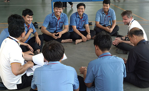mehrere Männer aus Deutschland und Thailand sitzen auf dem Boden im Kreis und sprechen miteinander