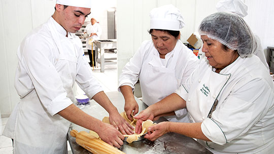 Szene einer Trainingsmaßnahme: Ausbilderin mit zwei Absolventen beim Backen