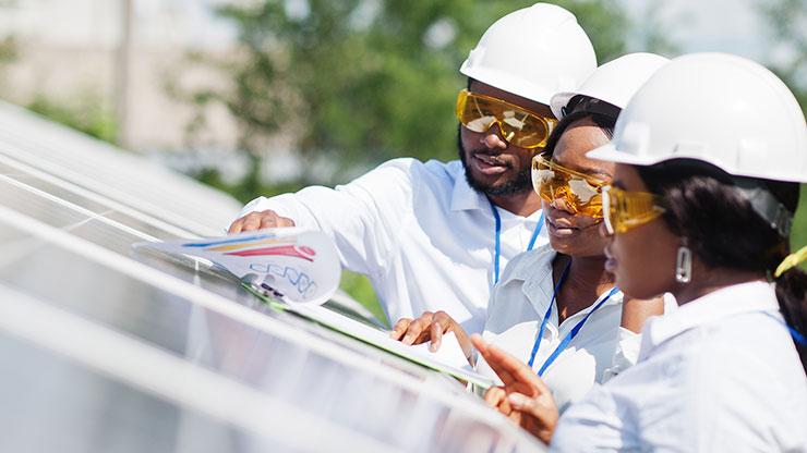drei afrikanische Personen stehen an einer Solarstation und prüfen Solarzellen