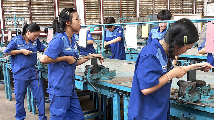 mehrere laotische junge Männer und Frauen bearbeiten Metallstücke mit einer Metallfeile