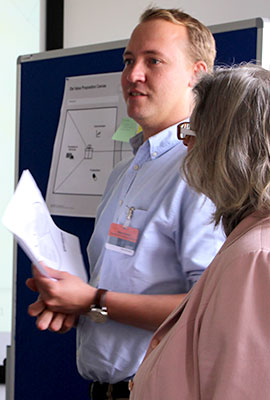 Teilnehmer und Teilnehmerin stehen an Pinwand und erläutern etwas