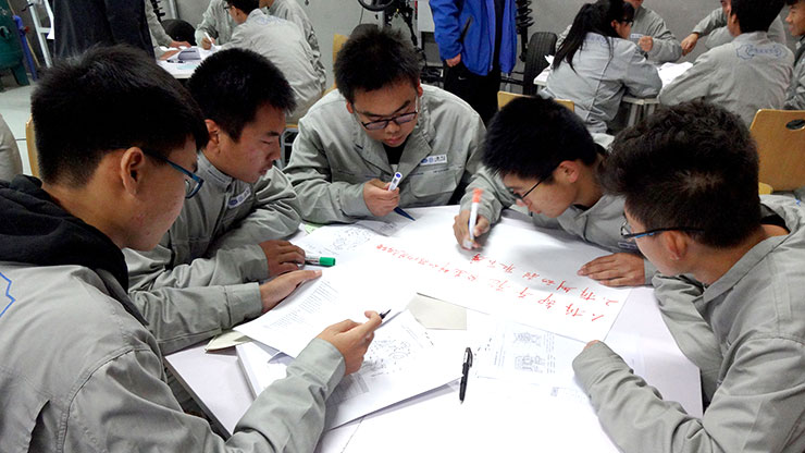 drei Chinesen beugen sich über Papierbogen auf dem Tisch