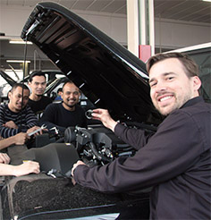 junge Männer stehen um ein Auto mit geöffneter Motorhaube und lächeln in die Kamera
