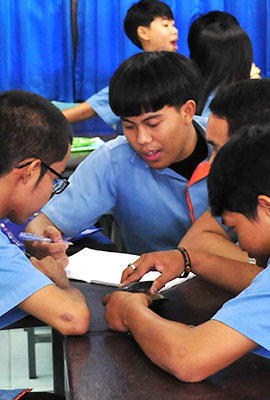 junge Thais sitzen um Tisch und untersuchen gemeinsam einen Gegenstand