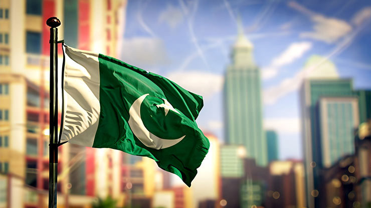 Nationalflagge Pakistans weht vor blassem Hintergrund von hohen städtischen Gebäuden