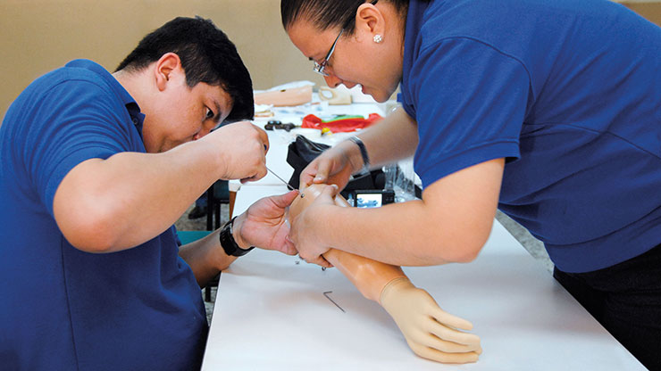 Auszubildender aus Lateinamerika arbeitet unter Anleitung einer Trainerin an einer Armprothese 
