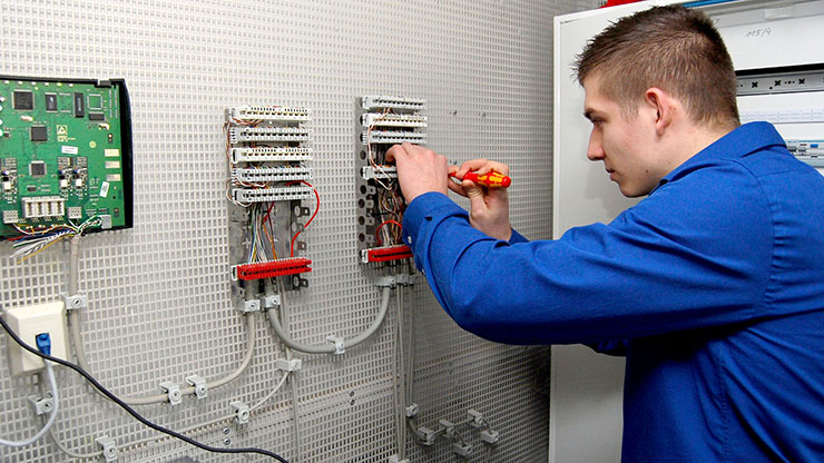 polnischer Praktikant arbeitet an einem Elektropanel an der Wand