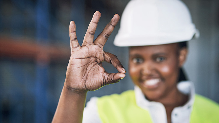 mutmaßlich afrikanische Frau trägt einen Bauhelm und formt mit einer Hand ein OK-Zeichen