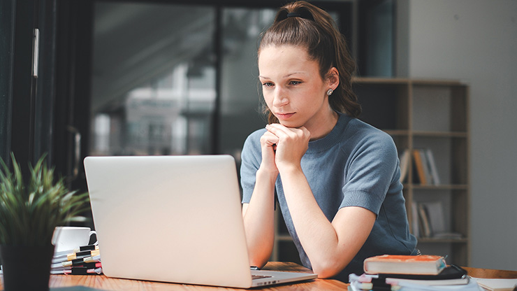 junge Frau sitzt an einem Tisch und schaut aufmerksam auf den Bildschirm eines Laptops