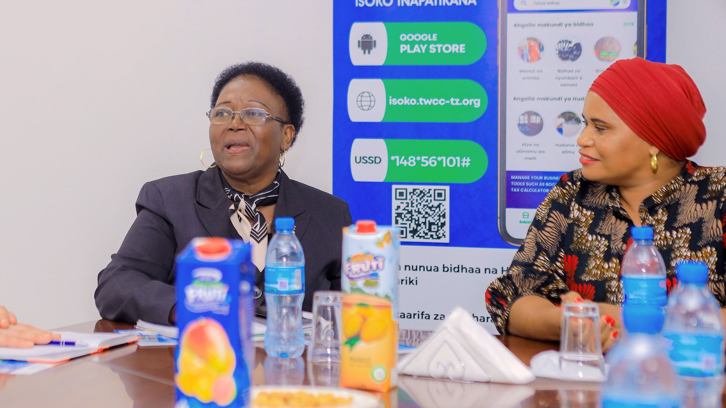 Two Tanzanian women sit at the table, lady on the left speaks